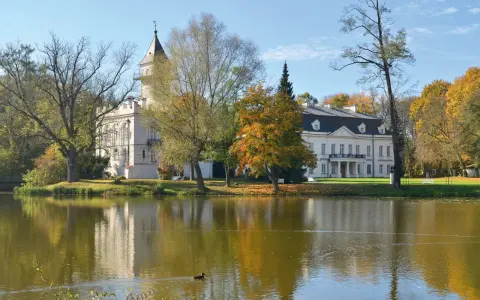 Pałac w jesiennej scenerii nad jeziorem, część Bolimowskiego Parku Krajobrazowego. Kaczka pływa po wodzie.