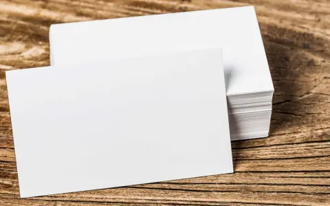 Pila de tarjetas de visita blancas sobre madera. Se aprecian los diferentes grosores de papel en la pila.