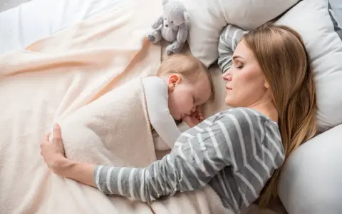 Mamma e bimbo dormono abbracciati, un tenero momento di co sleeping con un orsetto di peluche.