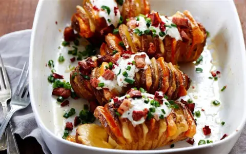 Pyszny obiad z ziemniaków: pieczone ziemniaki Hasselback z chrupiącym boczkiem, śmietaną i szczypiorkiem.