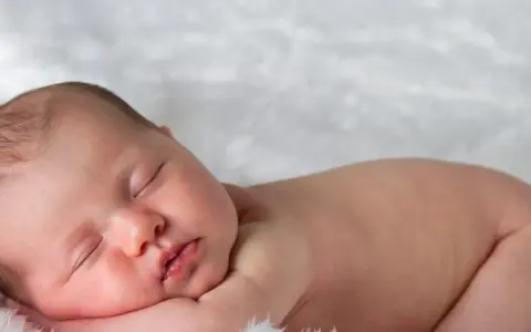 Śpiące, 3 miesięczne dziecko z delikatnymi włoskami, wtulone w miękkie futerko.