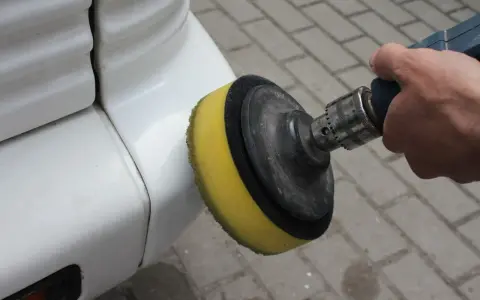 Ręka trzyma polerkę z żółtą gąbką, która poleruje biały zderzak. Dowiedz się, jak wypolerować samochód.