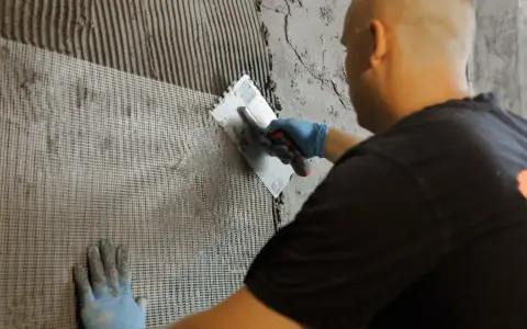 Mann verputzt Wand mit Armierungsgewebe. Perfekt für den Ausbau des Kellers.