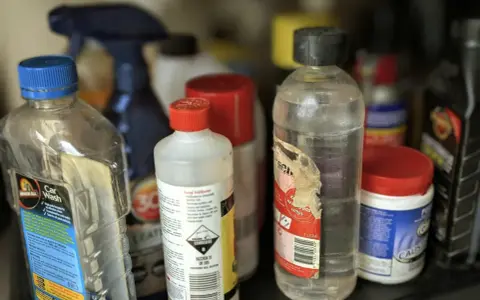 Na półce stoją różne butelki z płynami. Jedna z nich, z etykietą "Car Wash", sugeruje, gdzie wylać rozpuszczalnik, jeśli jest to konieczne.