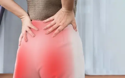 Kobieta trzyma się za bolące biodra i dolną część pleców, gdzie widoczne są czerwone plamy. To mogą być objawy korzonków.