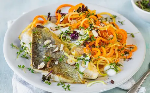 Gebratenes Fischfilet mit Spiralnudeln aus Karotten und Zucchini, garniert mit Kräutern und Mandelsplittern. Perfekt für leichte fasten rezepte.