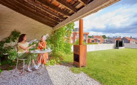 Due donne brindano su un terrazzo con prato. Sullo sfondo, una pompa di calore sul tetto.