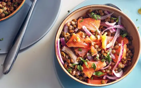 Salade de lentilles savoureuse avec des morceaux de saumon, des oignons rouges et du persil frais. Un plat coloré et nutritif.