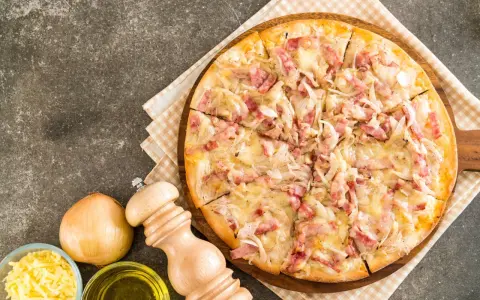 Flammekueche gourmande, garnie de lardons et d'oignons sur une base de fromage blanc crémeux. Un délice croustillant.