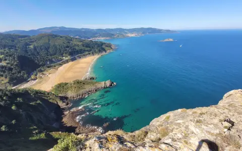 Blick vom Berg auf eine Bucht mit Sandstrand und türkisfarbenem Meer. Perfekt für eine Wanderung im Baskenland.