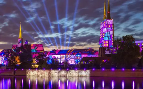 Ostrów Tumski we Wrocławiu nocą, rozświetlony kolorowymi projekcjami i niebieskimi snopami światła.