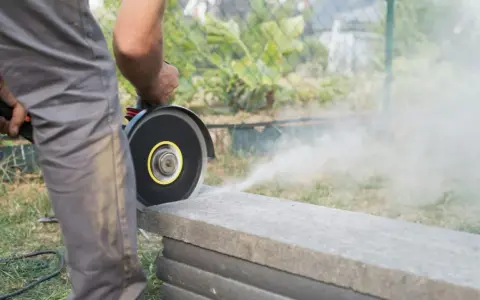 Mann schneidet mit Winkelschleifer Terrassenplatten. Staub wirbelt auf.