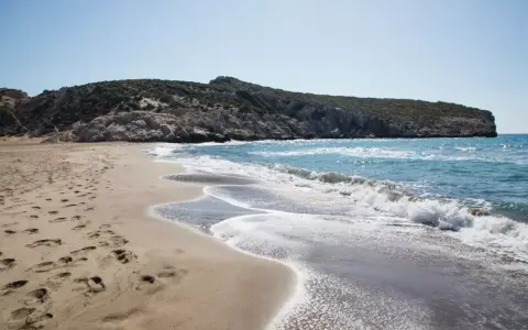 Piękne turcja plaże z piaszczystym brzegiem i skalistym wzgórzem w tle. Fale delikatnie rozbijają się o brzeg.