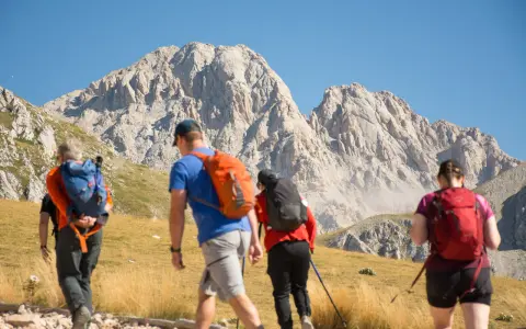 Escursionisti si dirigono verso un imponente corno grande, con zaini colorati e bastoncini da trekking.
