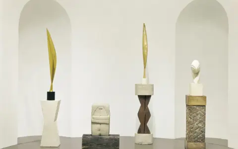 Rzeźby inspirowane twórczością **Constantin Brâncuși**: złoty liść, kamienna postać, drewniany rdzeń i biała głowa.