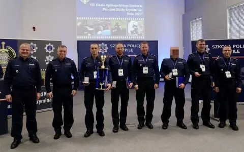 Policjanci w mundurach stoją w rzędzie, niektórzy trzymają nagrody i dyplomy.