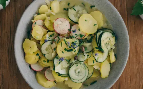 Kartoffelsalat mit Schale, garniert mit Radieschen, Gurken und Schnittlauch. Ein herzhaftes Gericht, das an Omas Küche erinnert.