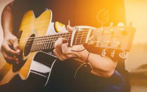 Osoba gra na gitarze akustycznej. Zastanawiasz się, ile trwa nauka gry na gitarze? To zależy od Ciebie!