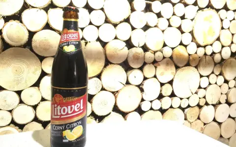 Butelka piwa Litovel Černý Citron na tle drewnianej ściany z plastrów drewna.