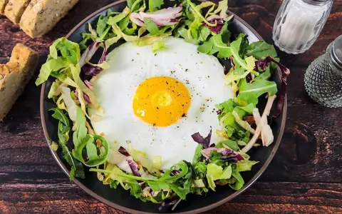 Un uovo occhio di bue su un letto di insalata mista, servito con pane integrale e condimenti.