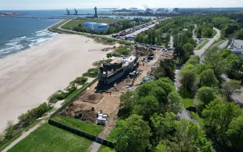 Gdańsk deptak nad morzem w budowie. Nowoczesny obiekt powstaje tuż przy plaży, w tle port i przemysłowe krajobrazy.