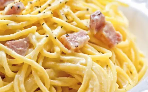Cremige Spaghetti Carbonara, nur mit Eigelb zubereitet, garniert mit Speckwürfeln und schwarzem Pfeffer.