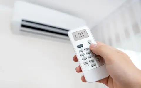 Mano ajustando el aire acondicionado a 21°C en modo "Cooling". La pantalla del control remoto muestra la temperatura y el modo, indicando que significa "cool" en el aire acondicionado: enfriar.