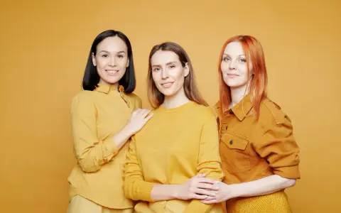 Trzy uśmiechnięte kobiety w stylizacjach w odcieniach koloru musztardowego.