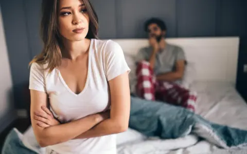 Kobieta zmartwiona, mężczyzna w tle. Problemy intymne, może uczulenie na spermę?