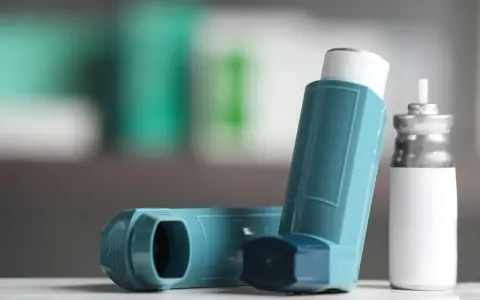 Zwei Inhalatoren, einer davon ein Symbicort-Spray, liegen auf einer weißen Oberfläche.