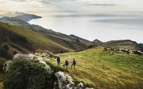 Trzech turystów podczas trekkingu na zielonym wzgórzu z widokiem na morze i góry.
