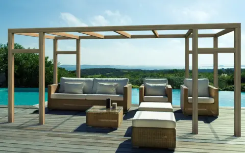 Salon extérieur avec mobilier en rotin sous une pergola en bois. La hauteur de la pergola en bois offre une ombre agréable sur la terrasse en bois, près de la piscine.