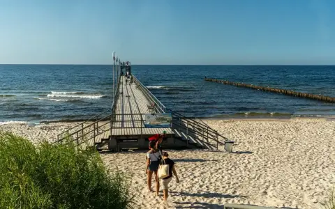 Sianożęty atrakcje: drewniane molo wchodzi w morze, plaża i fale.