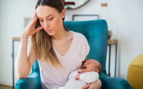 Zmęczona mama z płaczącym niemowlakiem na rękach, w fotelu, w poszukiwaniu siebie.