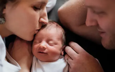 Mutter küsst ihr Neugeborenes, Vater schaut liebevoll zu. Diese Momente sind unbezahlbar, auch nach 1000 Tagen.