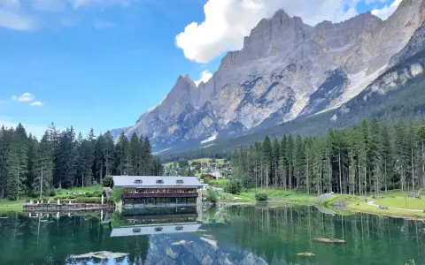 Riflessi alpini sul lago di Mosigo, con un rifugio e montagne imponenti sullo sfondo.