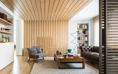 Elegante parete divisoria in legno fai da te, con doghe verticali illuminate, che separa un'accogliente zona living con divano in pelle e poltrona.