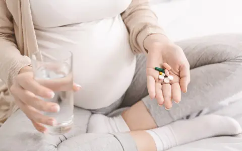 Ciężarna kobieta trzyma garść tabletek i szklankę wody, szukając odpowiedzi na pytanie: co na katar w ciąży.