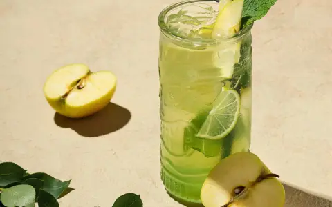 En uppfriskande p2 drink med äpple, lime och mynta. Två halvor av ett grönt äpple ligger bredvid glaset.