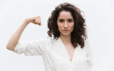 Kobieta pokazuje biceps, symbolizując siłę. Może to być metafora objawów wysokiego testosteronu, takich jak pewność siebie i determinacja.
