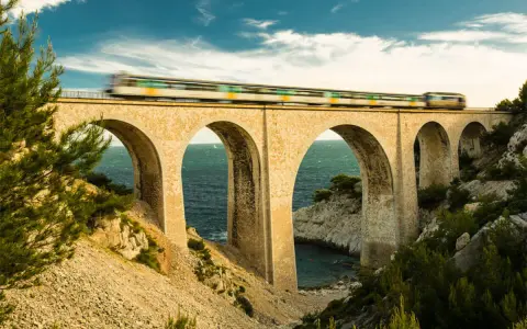 Ein Zug rast über eine Bogenbrücke, die Teil des Bahnnetz Frankreichs ist. Das Meer glitzert unter den Bögen.