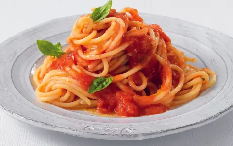 Un piatto di pasta fatta in casa, spaghetti al pomodoro fresco e basilico, serviti su un piatto rustico.