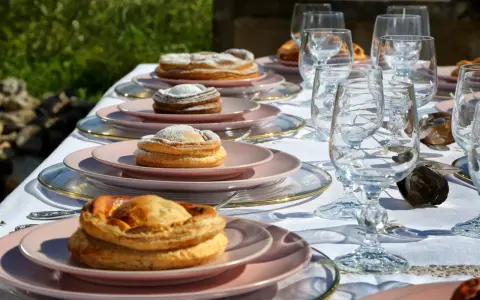 Tavola apparecchiata con bicchieri di cristallo e piatti rosa, su cui riposano dolci invitanti, tra cui una piscialetta leccese cosparsa di zucchero a velo.