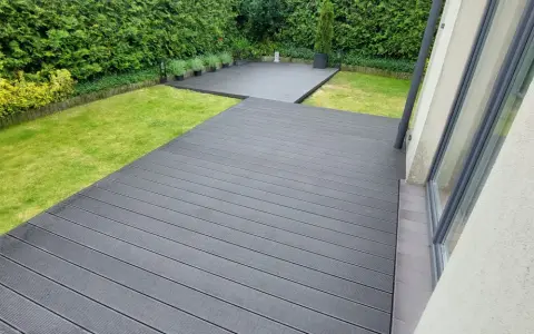 Nowoczesna deska kompozytowa antracyt tworzy elegancką przestrzeń wokół domu, otoczoną zielenią.
