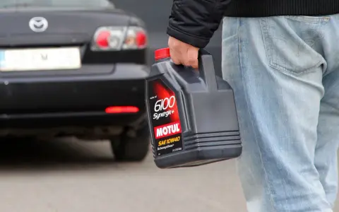 Mężczyzna niesie kanister z olejem silnikowym Motul. W tle czarna Mazda.