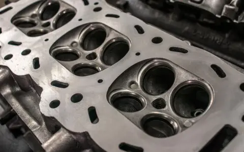 Nahaufnahme eines Zylinderkopfs eines Autos. Die Ventilsitze und die Bohrungen für die Zündkerzen sind sichtbar. Eine neue Kopfdichtung für das Auto wird bald montiert.
