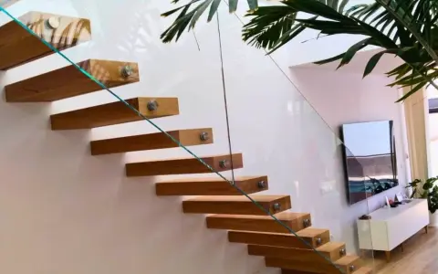 Escalera flotante de madera con **rejas de cristal** que aportan ligereza y modernidad al espacio.