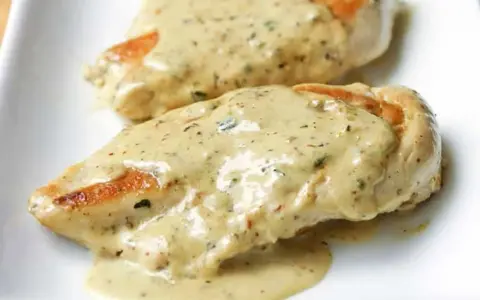Deux morceaux de poulet à la crème, nappés d'une sauce onctueuse aux herbes, sur une assiette blanche.