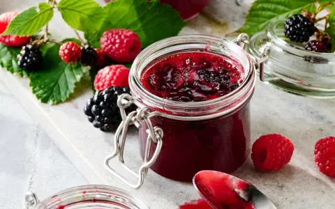 Frische Brombeeren und Himbeeren neben einem Glas selbstgemachter Marmelade. Perfekt für brombeeren rezepte schnell und einfach.