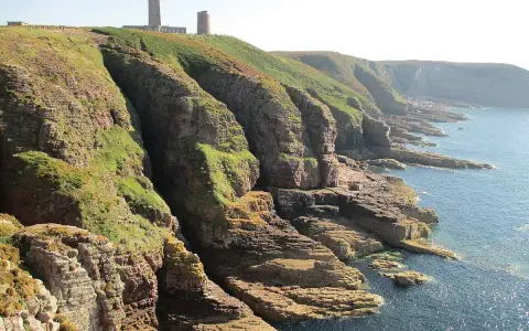 Scogliere verdi e rocciose con un faro in cima. Ideale per consigli su **Bretagna in moto**.